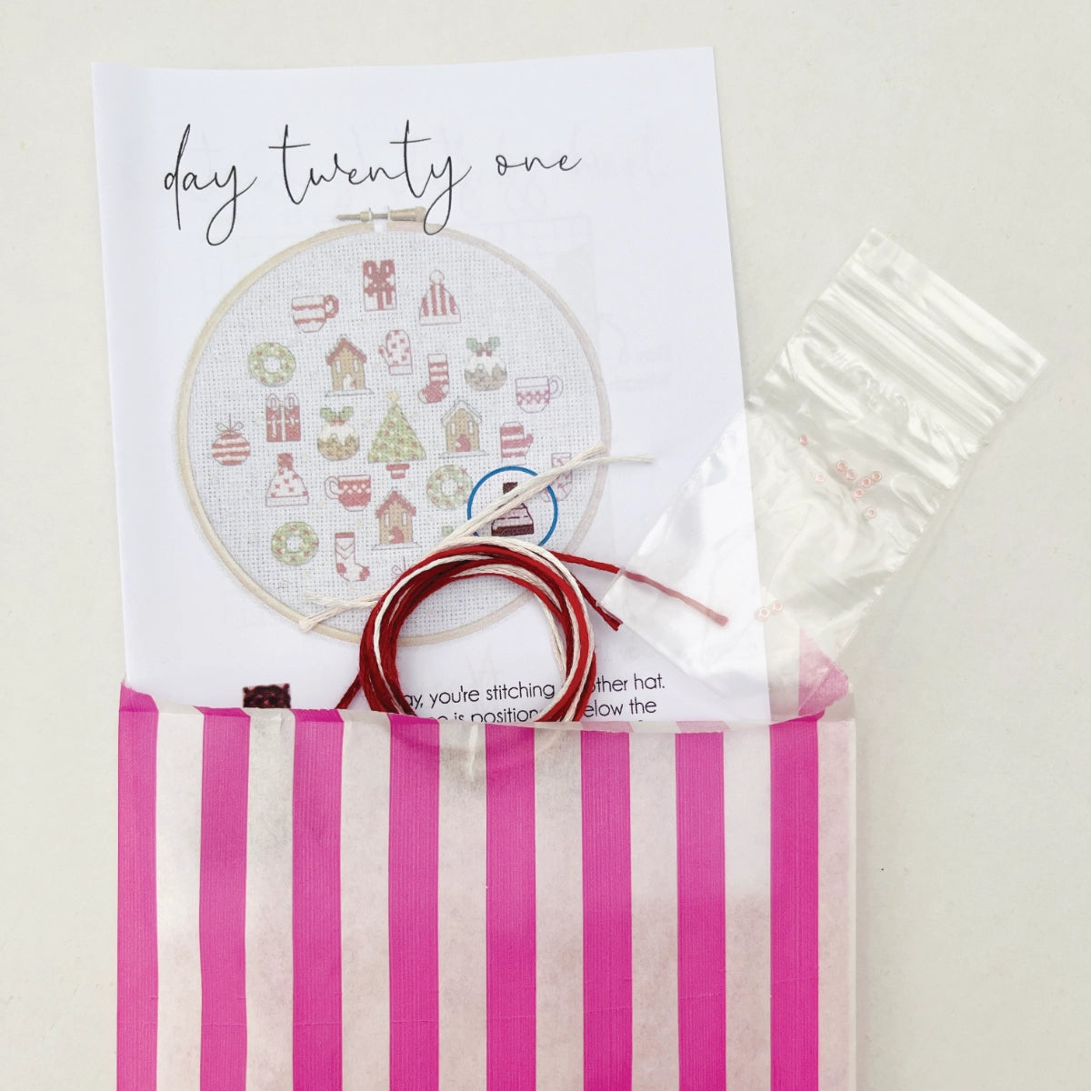 Daily materials from the Advent Calendar Cross Stitch Kit – stranded cotton threads, seed beads and instruction booklet inside a paper bag.