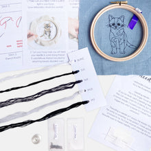 Load image into Gallery viewer, Black Cat Embroidery Kit - Kirsty Freeman Design. The contents include: blue linen fabric (with the cat outline pre-stitched for you), an embroidery hoop, 2x needles, seed beads, an instruction booklet, and a selection of threads.
