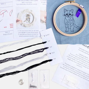 Black Cat Embroidery Kit - Kirsty Freeman Design. The contents include: blue linen fabric (with the cat outline pre-stitched for you), an embroidery hoop, 2x needles, seed beads, an instruction booklet, and a selection of threads.