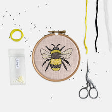 Load image into Gallery viewer, Bumble Bee Embroidery Kit - Kirsty Freeman Design. Modern embroidery hoop with bee emblem stitched onto pink linen fabric, surrounded by embroidery materials.
