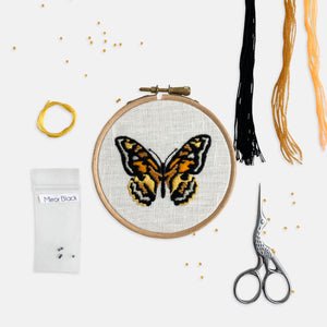 Mustard Yellow Butterfly Embroidery Kit - Kirsty Freeman Design. Seed beads and satin stitch in black and shades of orange have been used to embroider a butterfly onto white linen fabric, and presented in an embroidery hoop.