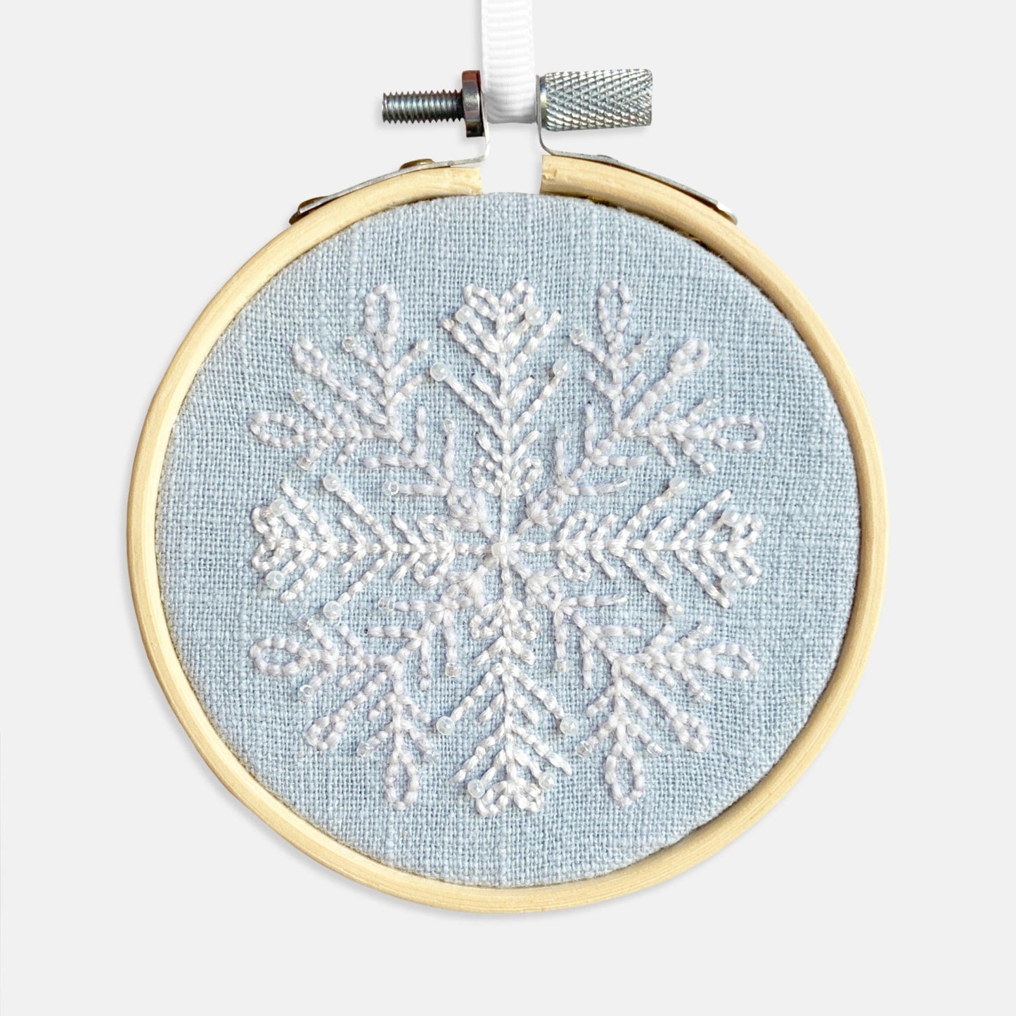 Snowflake Embroidery Kit - Kirsty Freeman Design. The snowflake pattern has been stitched using backstitch in white thread, onto blue linen fabric and framed in an embroidery hoop.