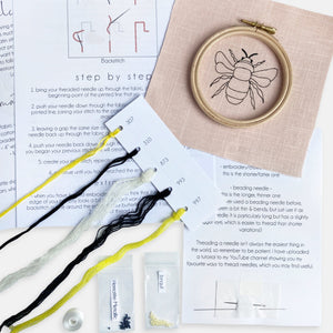 Bee Embroidery Kit Designed and Made in the UK - Kirsty Freeman Design. A closer look at the simple embroidery kit contents: instructions with diagrams, pink linen fabric with a stitched bee outline, an embroidery hoop, needles, beads and a selection of threads.