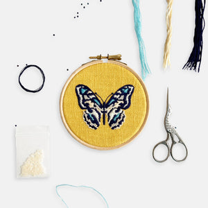 Butterfly Embroidery Kit - Kirsty Freeman Design. A colourful completed embroidery hoop design of a butterfly, surrounded by the contents of the embroidery kit.