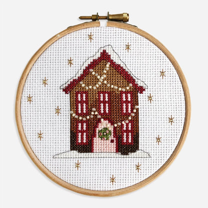 Close-up of finished Gingerbread House cross stitch kit with red windows, a pink door and twinkly strings of fairy lights.