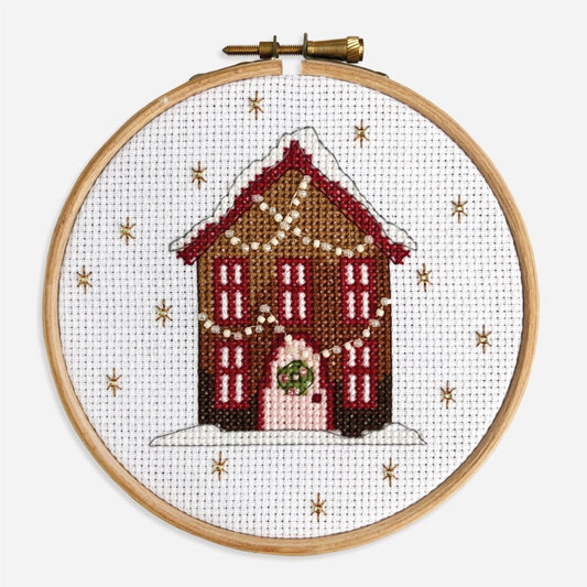 Close-up of finished Gingerbread House cross stitch kit with red windows, a pink door and twinkly strings of fairy lights.
