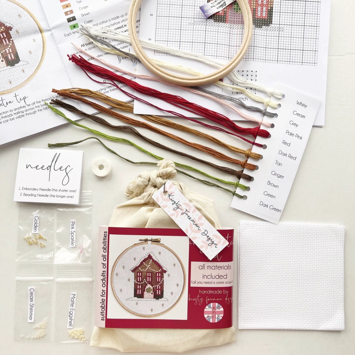 Gingerbread House Cross Stitch Kit packaging displayed with aida, embroidery hoop, threads, beads, needles, instructions and cross stitch charts.