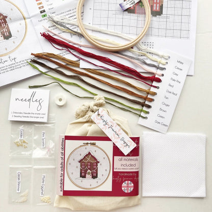 Gingerbread House Cross Stitch Kit packaging displayed with aida, embroidery hoop, threads, beads, needles, instructions and cross stitch charts.