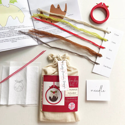 Christmas Pudding Embroidery Kit packaging with red hoop, fabric, threads, instructions, needle and ribbon to make festive DIY craft project.