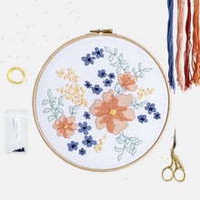 Load image into Gallery viewer, Flower Cross Stitch Kit - Kirsty Freeman Design. A botanical pattern stitched in shades of coral, blue , yellow and green, onto white aida fabric and presented in an embroidery hoop.
