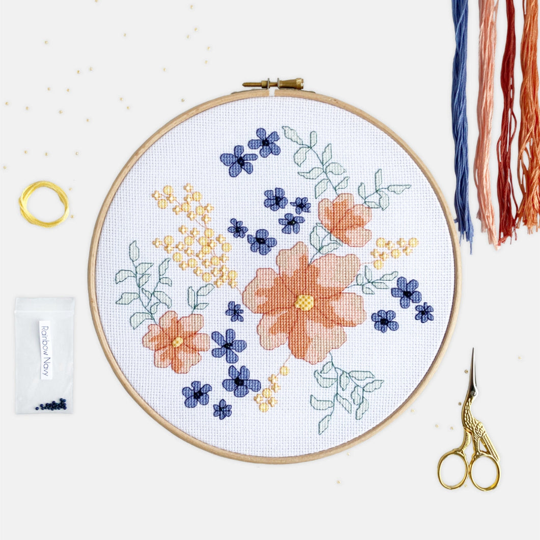 Flower Cross Stitch Kit - Kirsty Freeman Design. A botanical pattern stitched in shades of coral, blue , yellow and green, onto white aida fabric and presented in an embroidery hoop.