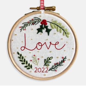Christmas Decoration Kits - Kirsty Freeman Design. Close up, the word Love is stitched in red thread, onto white fabric, surrounded by Christmas foliage and gold beads.