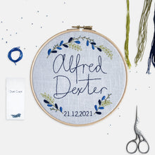 Load image into Gallery viewer, Personalised Baby Embroidery Kit - Kirsty Freeman Design. A finished embroidery, displayed inside a 7&quot; embroidery hoop, with a botanical wreath stitched around two names in the centre of the design.
