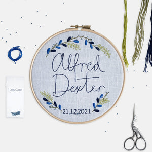 New Baby Embroidery Kit - Kirsty Freeman Design. The blue colourway of the personalised embroidery kit, with a stitched name, date and botanical details, stitched in shades of blue and green.