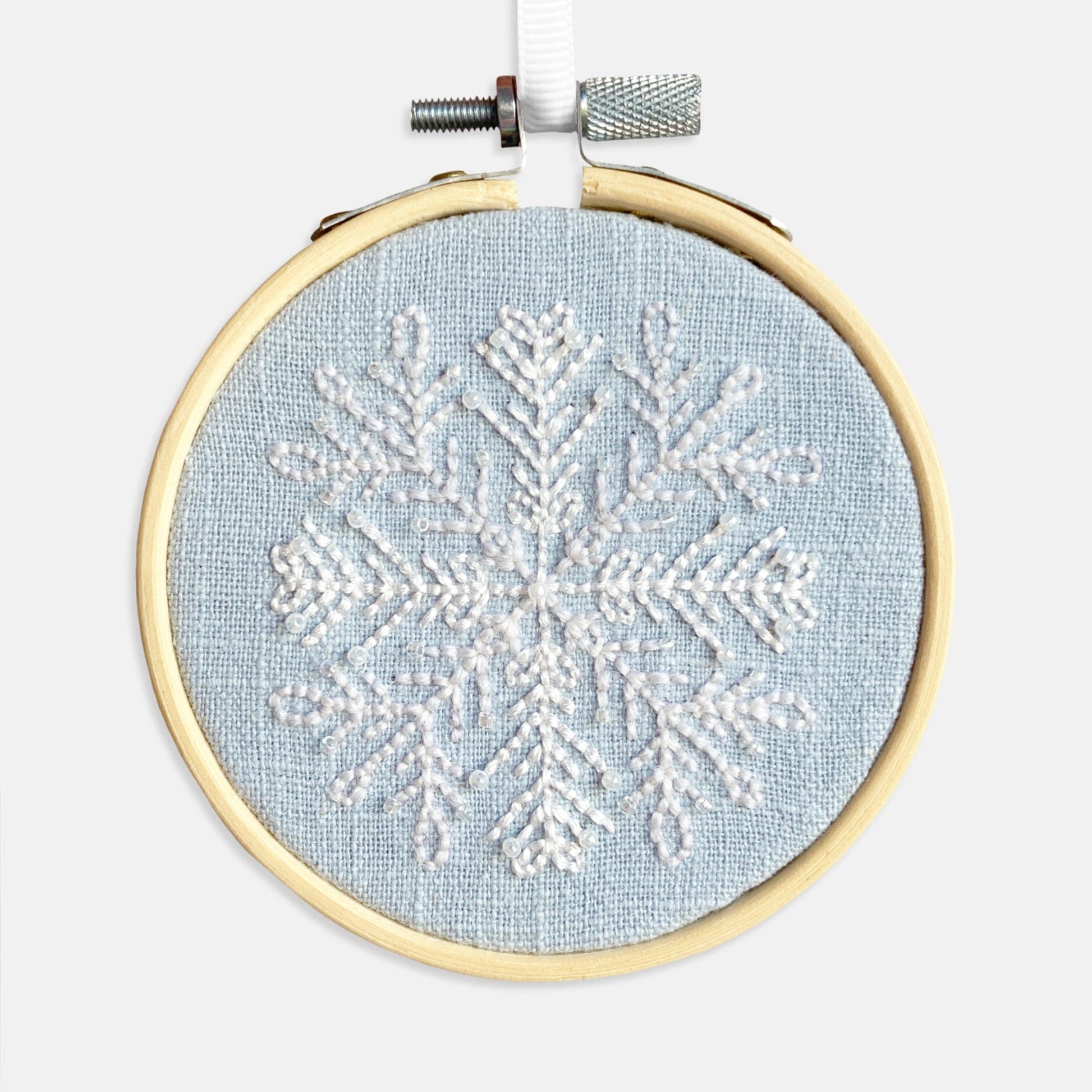 Snowflake Embroidery Kit - Kirsty Freeman Design. The snowflake pattern has been stitched using backstitch in white thread, onto blue linen fabric and framed in an embroidery hoop.
