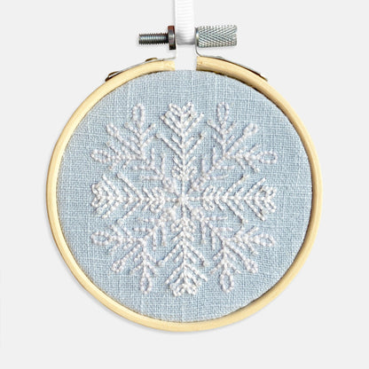 Snowflake Embroidery Kit - Kirsty Freeman Design. The snowflake pattern has been stitched using backstitch in white thread, onto blue linen fabric and framed in an embroidery hoop.