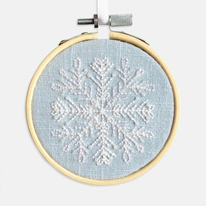 Snowflake Embroidery Kit - Kirsty Freeman Design. The snowflake pattern has been stitched using backstitch in white thread, onto blue linen fabric and framed in an embroidery hoop.