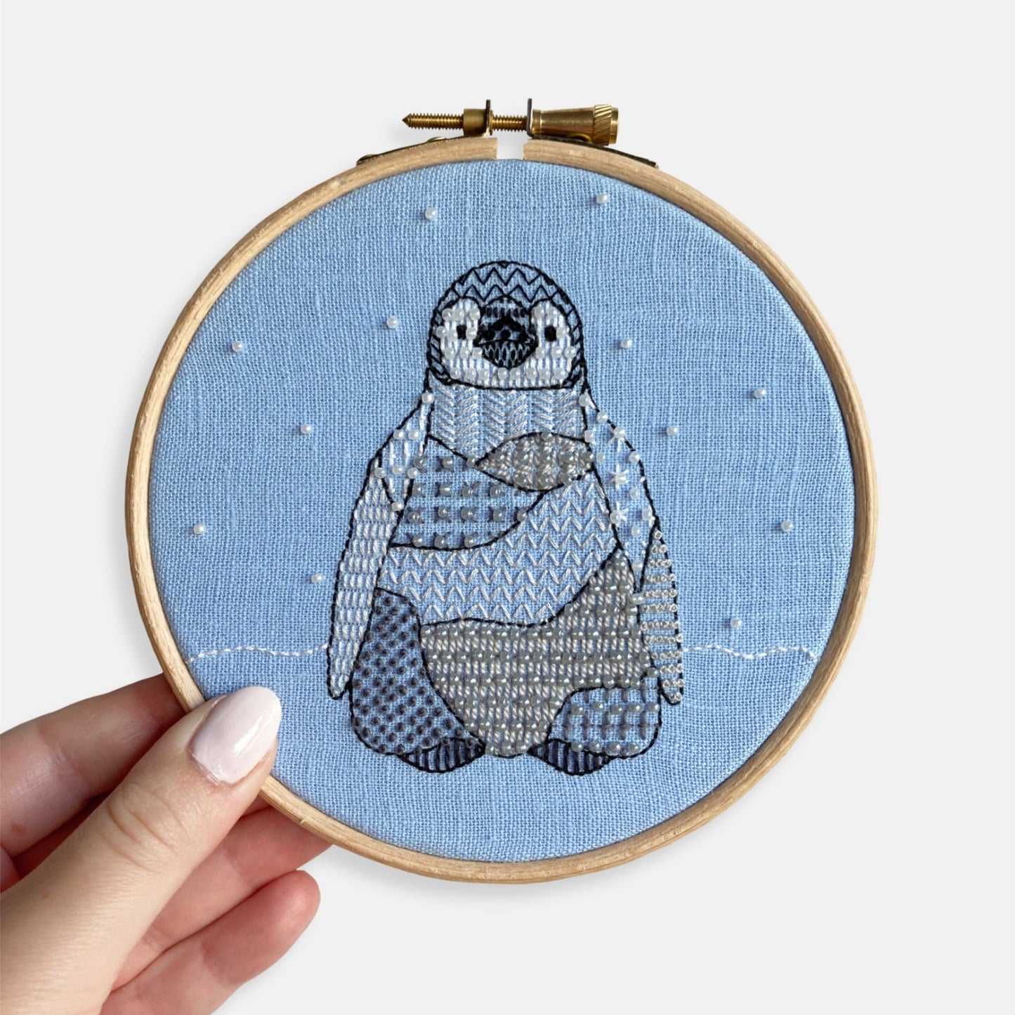 Penguin Embroidery Kit - Kirsty Freeman Design. An example of our finished embroidery kit animal character. The penguin is stitched onto blue linen and framed inside the embroidery hoop.