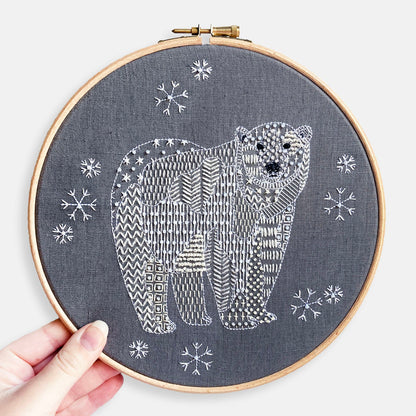 Polar Bear Embroidery Kit - Kirsty Freeman Design. The animal has been stitched onto dark grey linen using patterned geometric embroidery stitches. The polar bear is surrounded by snowflakes.
