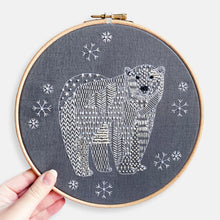 Load image into Gallery viewer, Polar Bear Embroidery Kit - Kirsty Freeman Design. The animal has been stitched onto dark grey linen using patterned geometric embroidery stitches. The polar bear is surrounded by snowflakes.

