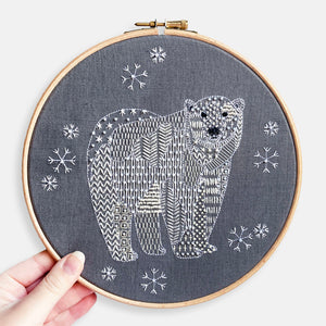 Polar Bear Embroidery Kit - Kirsty Freeman Design. The animal has been stitched onto dark grey linen using patterned geometric embroidery stitches. The polar bear is surrounded by snowflakes.